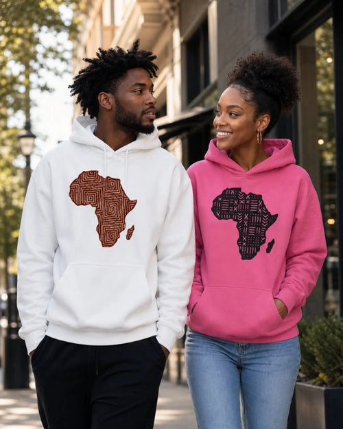 A man and a woman walking outdoors on a city street, each wearing a hoodie with a large African continent graphic on the chest. The man's hoodie is white with a brown graphic, and the woman's hoodie is bright pink with a black graphic.